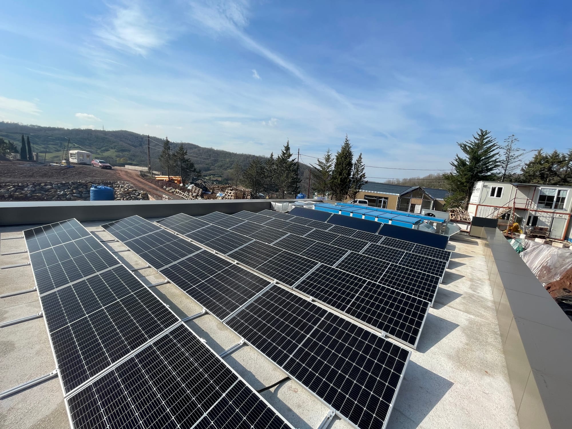 A flat roof covered in dark solar panels, with three wider collectors and rooftop plant beyond.