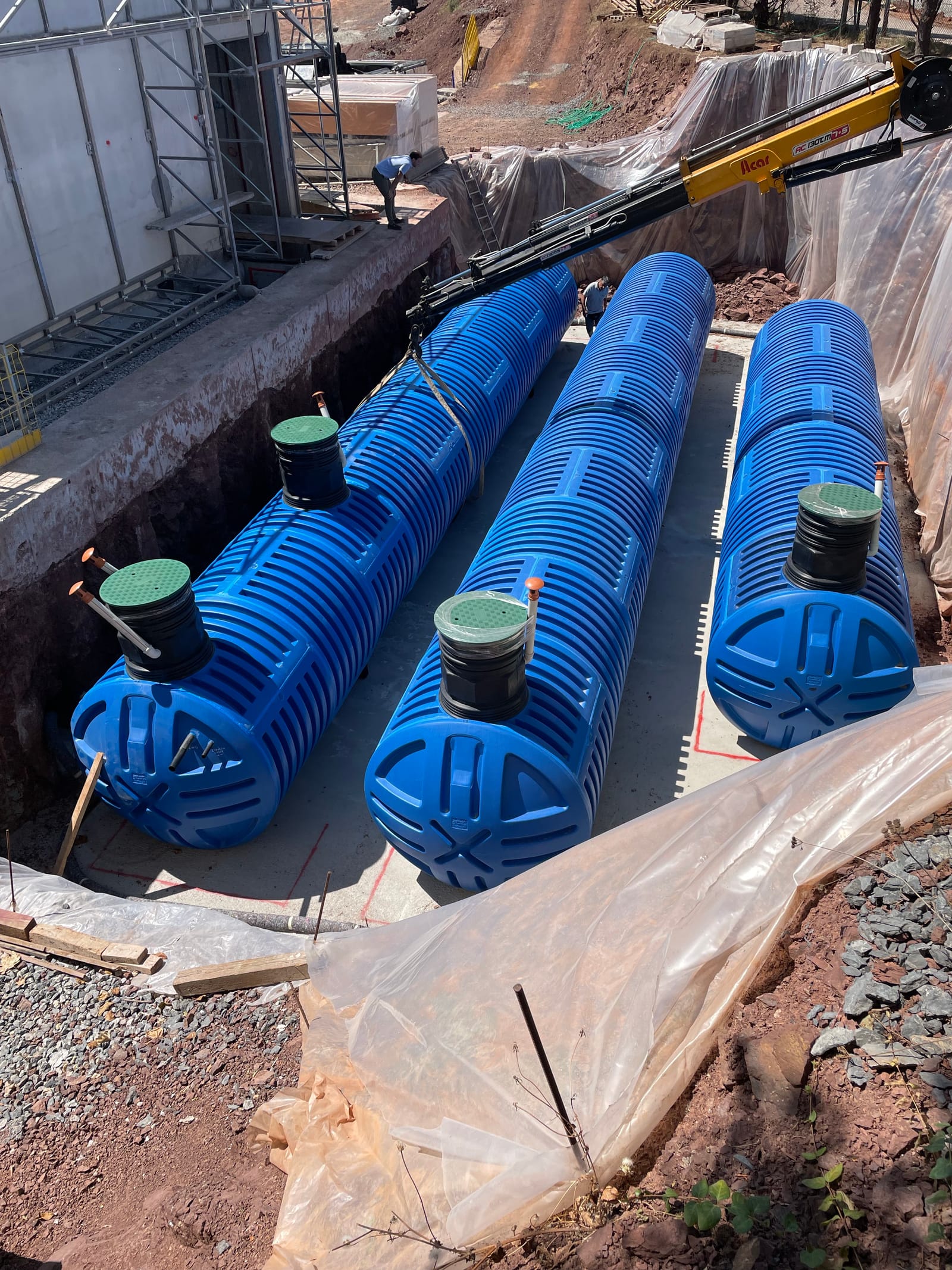 Three large blue cylindrical water tanks lying in an open excavation before being buried.