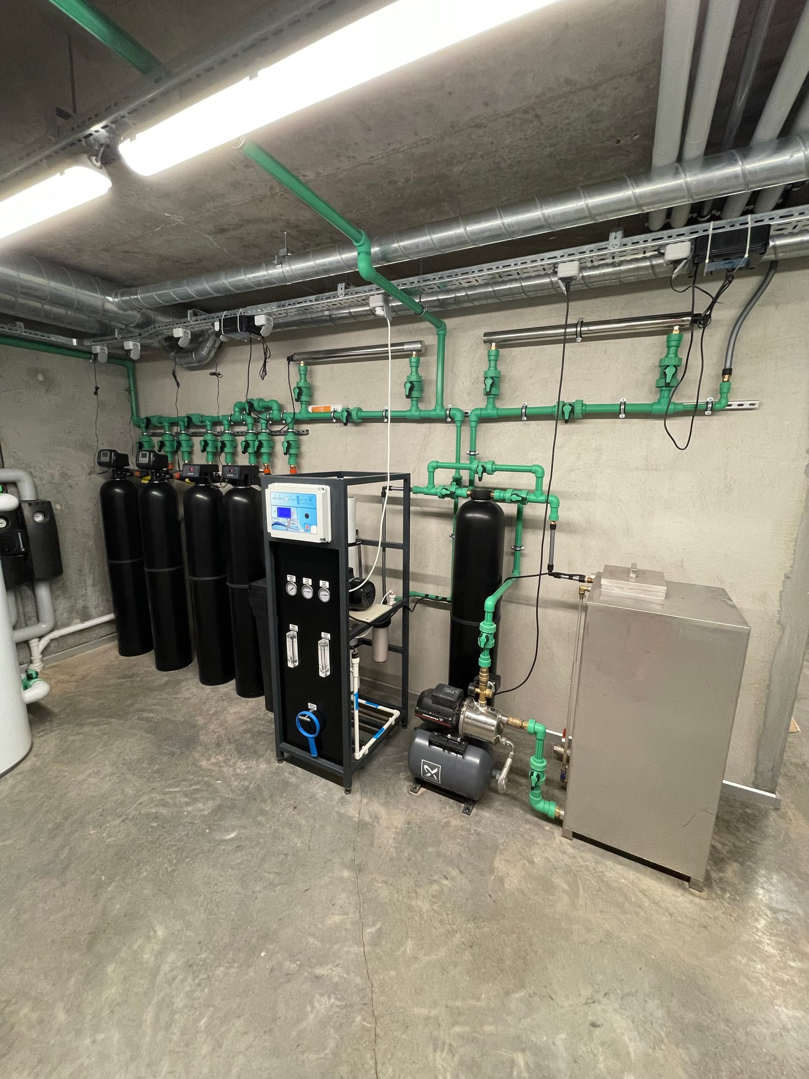 A water filtration installation with black pressure vessels, green pipework and a control panel.