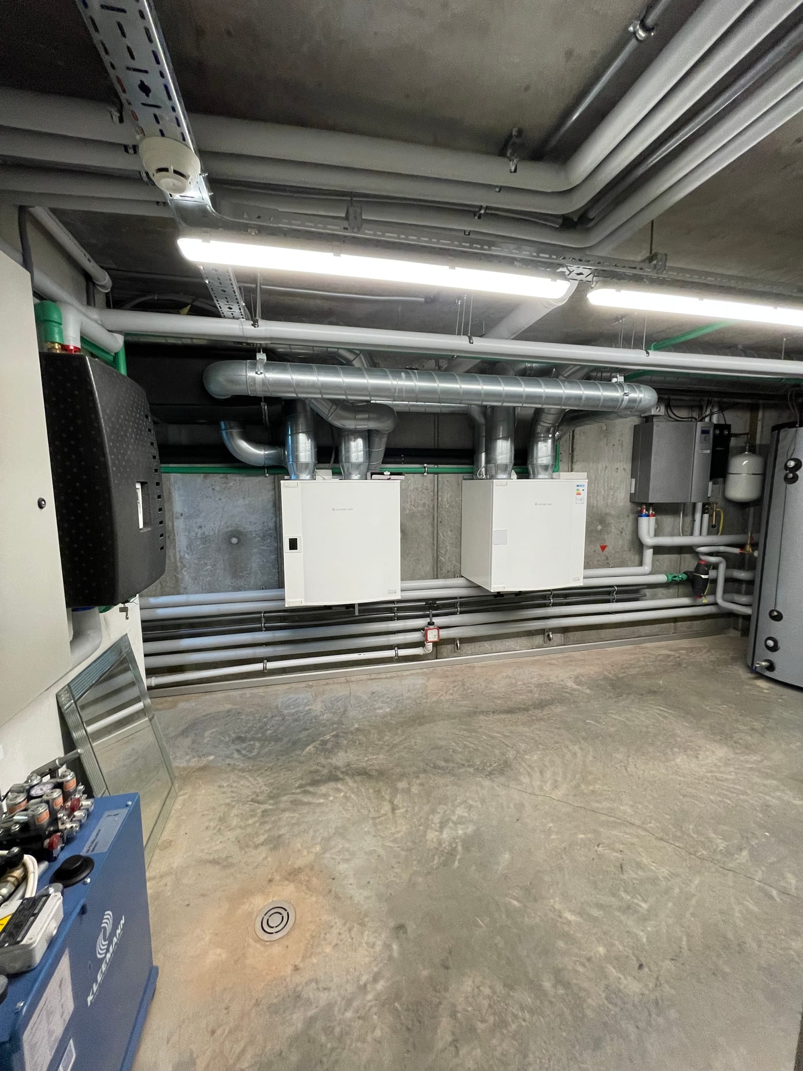 A concrete plant room containing ventilation units and insulated ductwork.