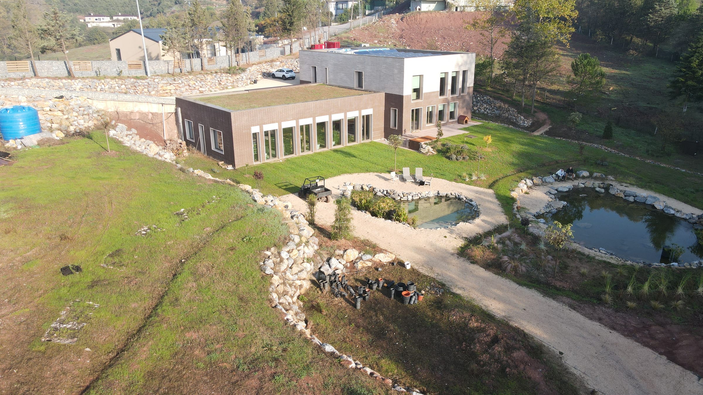 Aerial view of a building beside two ponds, with terraced ground and cut paths around them.