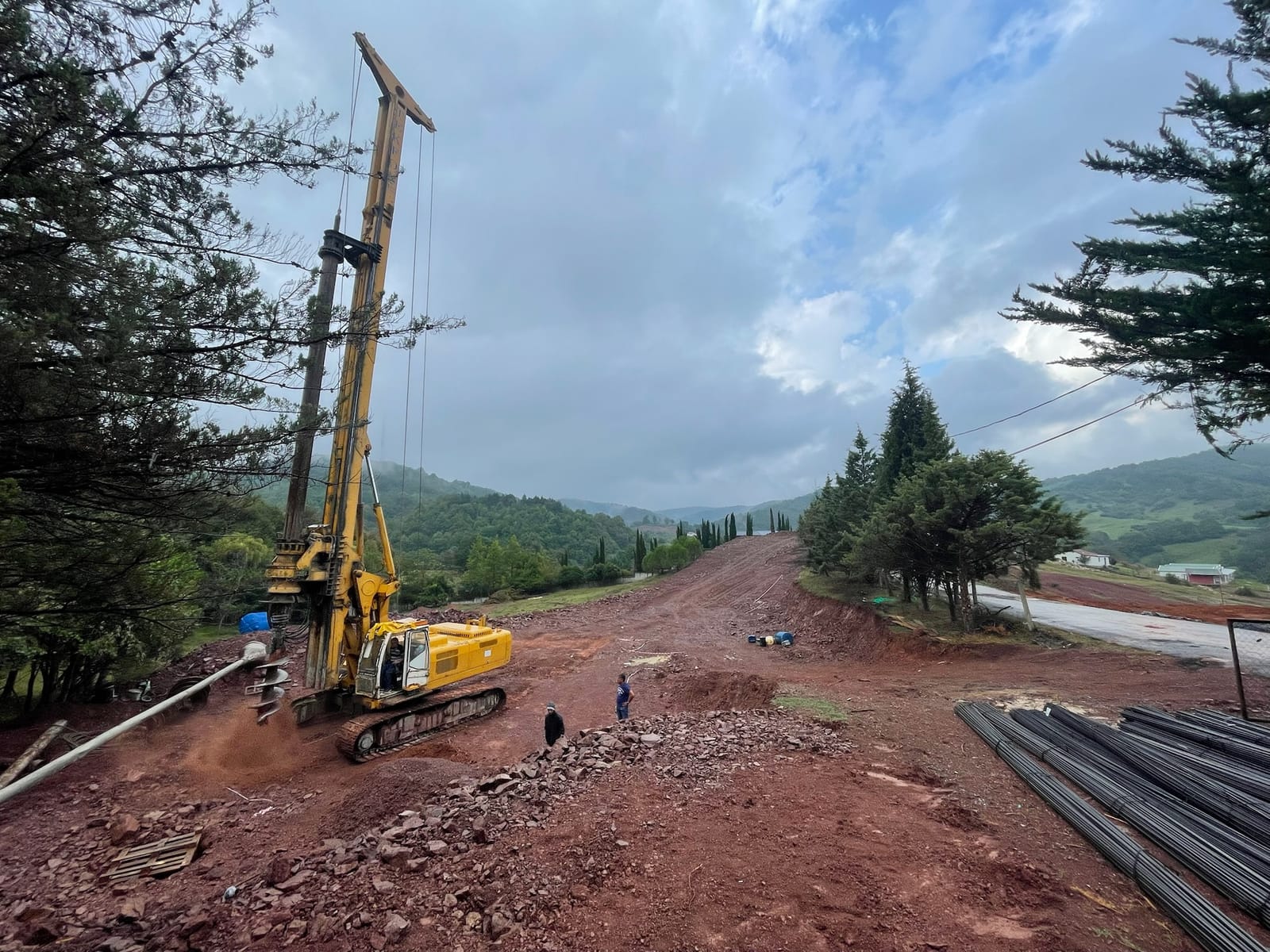 A yellow piling rig on a cleared red-earth site with trees behind.