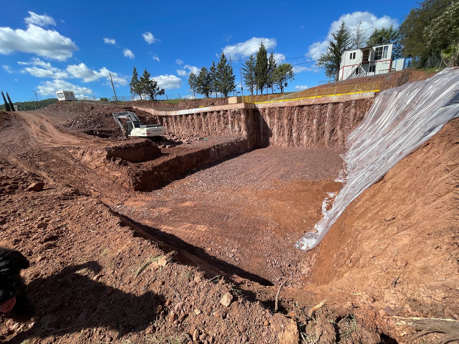 A deep excavation in red earth with plastic sheeting laid over the banks.