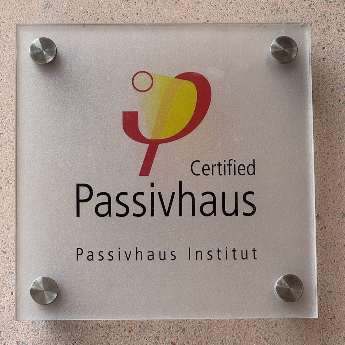 A glass plaque on a plastered wall reading Certified Passivhaus, Passivhaus Institut.