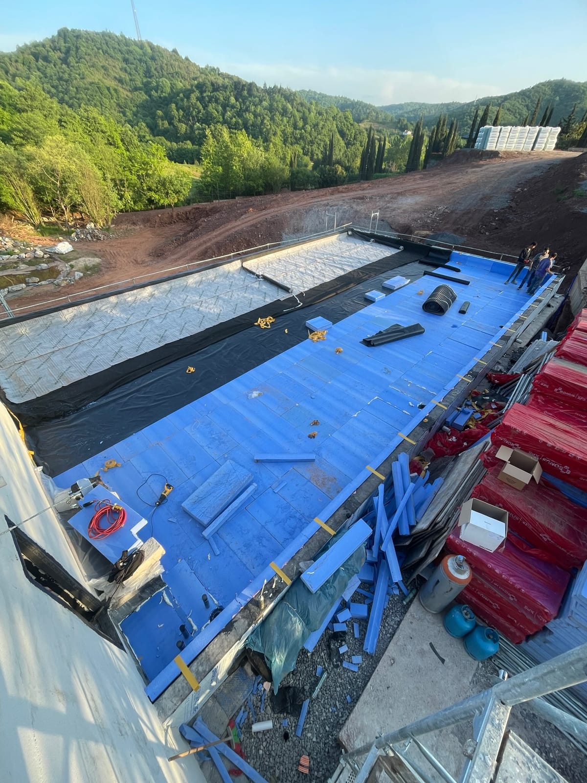 A flat roof under construction, partly covered with blue waterproofing membrane and insulation boards.