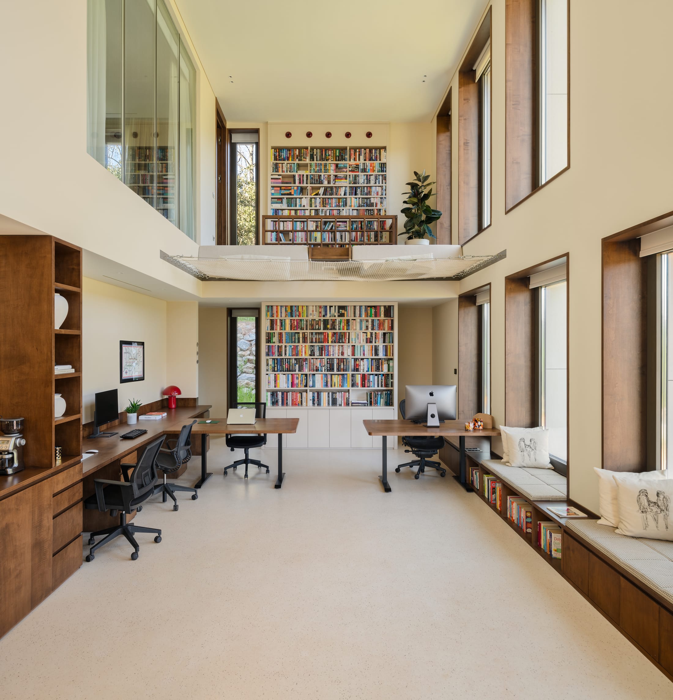 A double-height room lined with books, desks along one side and a reading platform suspended above.
