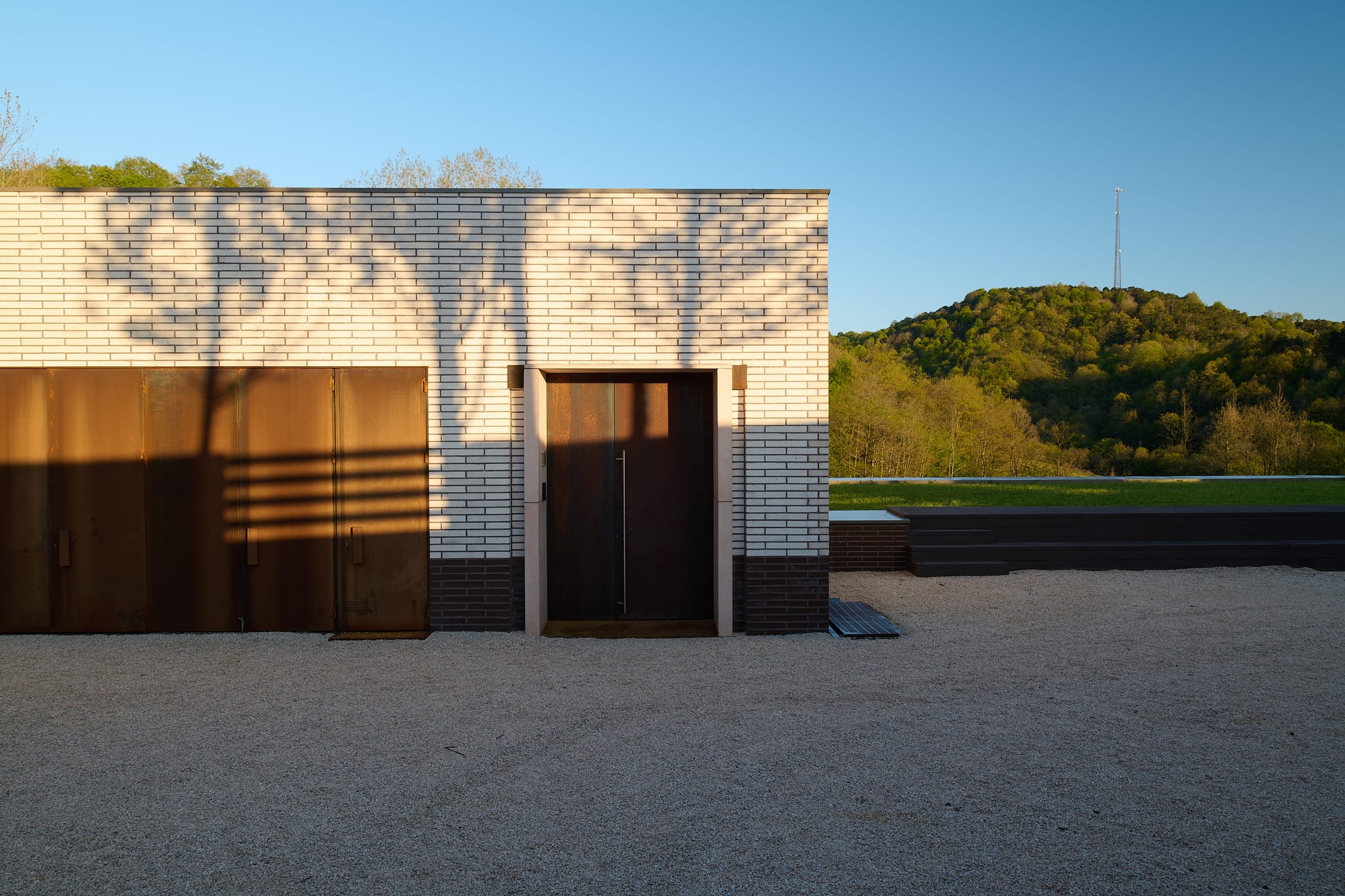A pale brick facade with two tall weathered-steel doors, seen across a gravel court.
