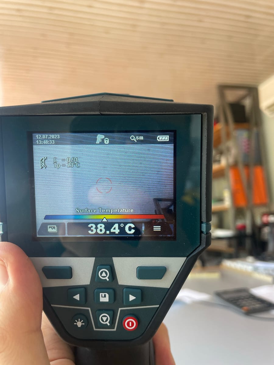 A handheld thermal imaging camera displaying a surface temperature reading of 38.4 degrees Celsius.